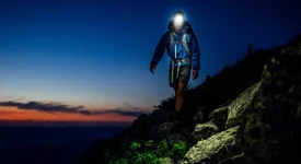 Un homme sur un sentier de montagne technique au crépuscule s'éclaire avec une lampe frontale.